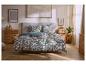 Chambre avec lit double et parure de lit florale verte, commode en bois et décoration minimaliste.