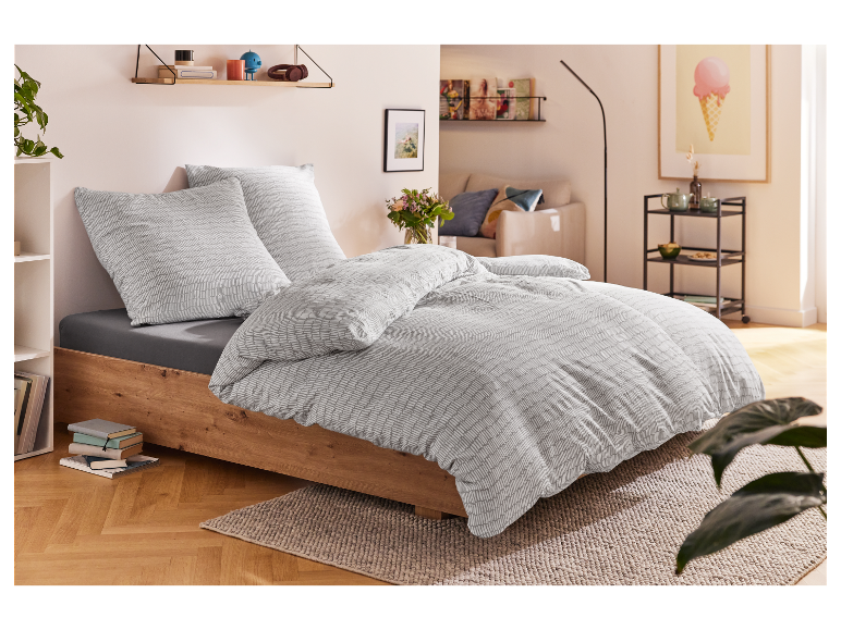 Parure de lit gris clair à motif de lignes ondulées sur un lit en bois.