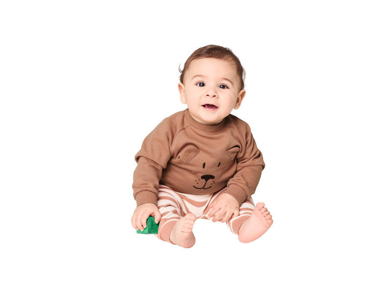 Bébé en haut marron à motif d'ours et pantalon rayé, tenant un jouet vert.