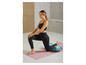 Une femme faisant du yoga sur un tapis rose avec un coussin bleu.