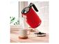 Bouilloire électrique rouge avec l'inscription «1973» versant de l'eau dans une tasse sur un comptoir en bois.