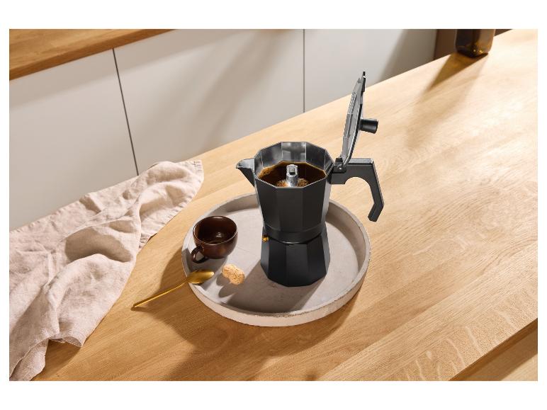 Cafetière moka noire avec café, une tasse et des biscuits sur un plateau sur un comptoir en bois.