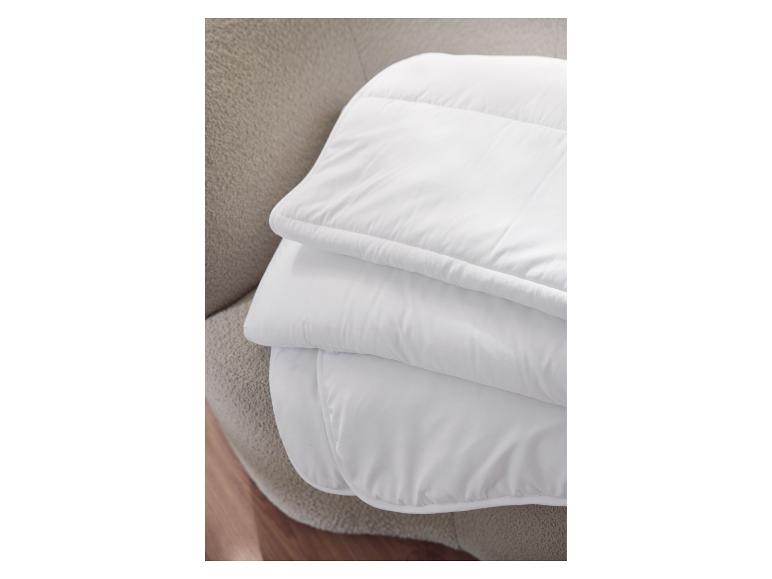 Couette blanche pliée sur une surface texturée beige.
