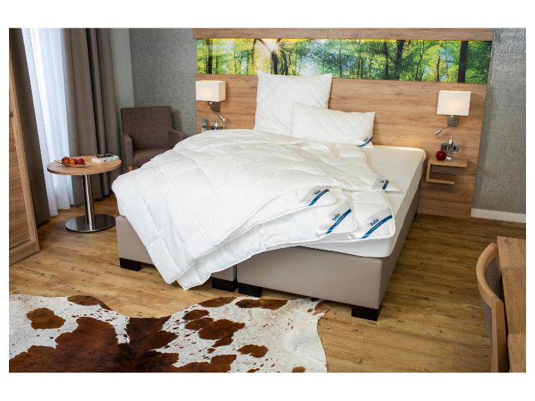 Chambre moderne avec lit, literie blanche BeCo, tables de chevet en bois et tapis en peau de vache.