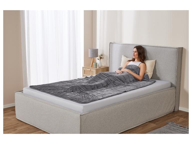 Femme relaxée au lit avec une couverture lestée grise.
