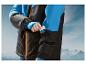 Une veste de ski noire avec des détails bleus, une personne met sa main dans une poche.