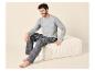 Homme en t-shirt gris à manches longues et pyjama rayé assis sur un pouf beige.