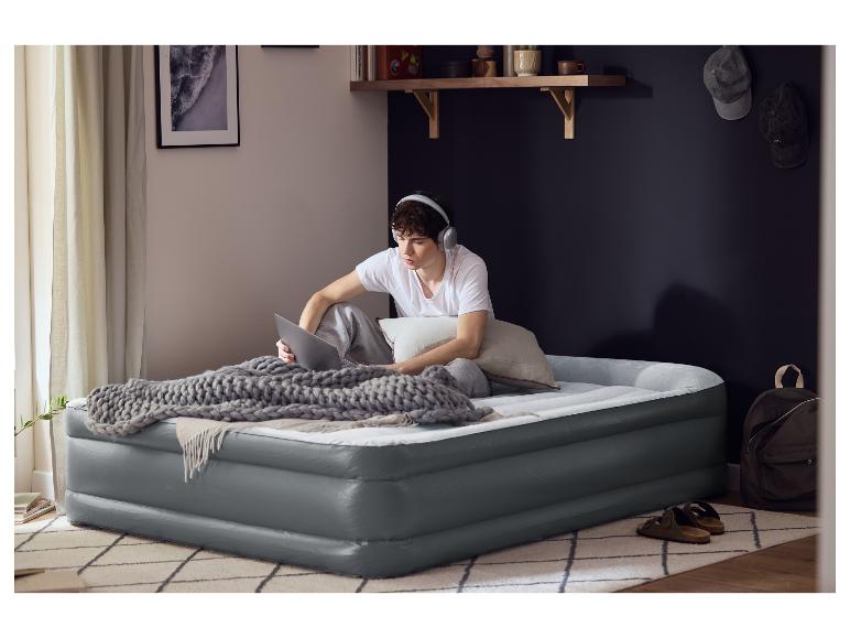 Un jeune homme assis sur un lit gonflable LIVARNO® Premium avec un ordinateur portable et un casque.