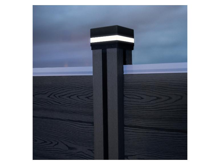 Poteau de clôture gris foncé avec lumière de capuchon éclairée contre un ciel crépusculaire.