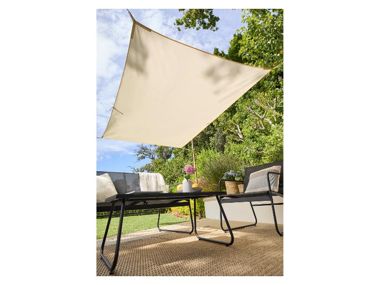 Patio avec voile d'ombrage, canapé d'extérieur et table basse sur un tapis tressé.