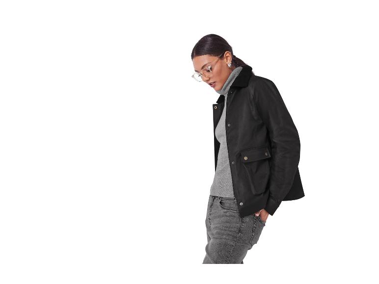 Femme en veste noire, pull gris et jean, avec des lunettes.