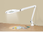 Lampe loupe blanche éclairant des fournitures de couture sur une table en bois.