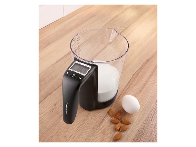 Pichet doseur avec balance numérique, lait, amandes et un œuf sur une surface en bois.