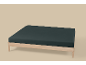 Lit simple en bois clair avec matelas foncé sur fond beige.
