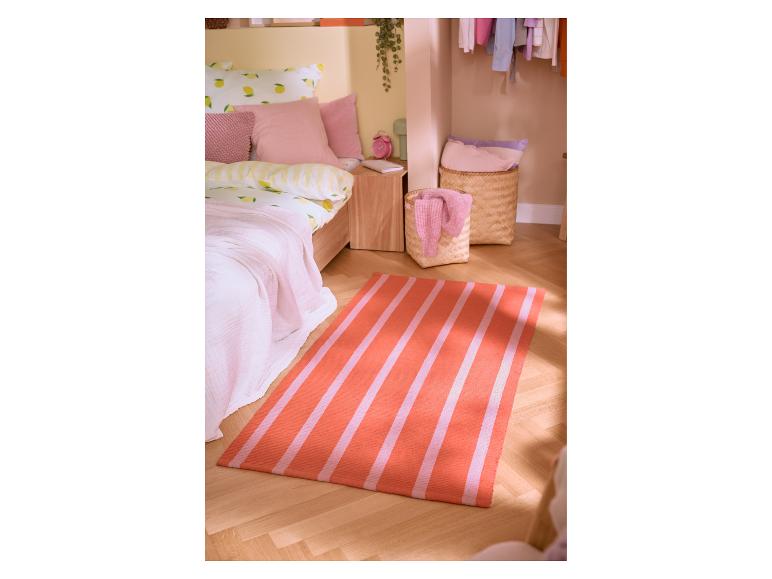 Chambre avec literie à motif de citrons, oreillers roses et tapis rayé orange et rose.