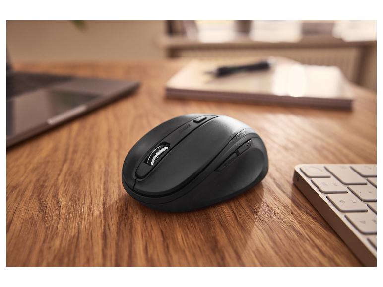 Souris sans fil noire sur une table en bois avec un ordinateur portable et un clavier en arrière-plan.