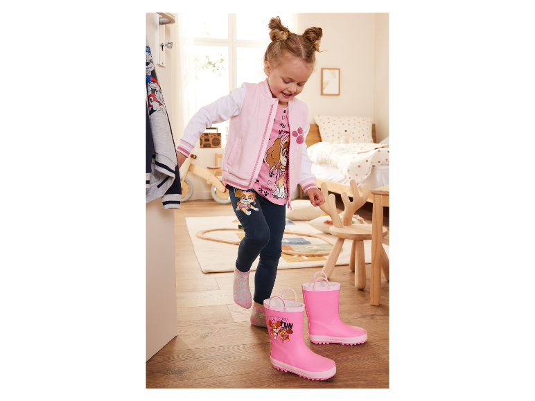 Petite fille essayant des bottes de pluie roses à l'effigie de Pat' Patrouille.