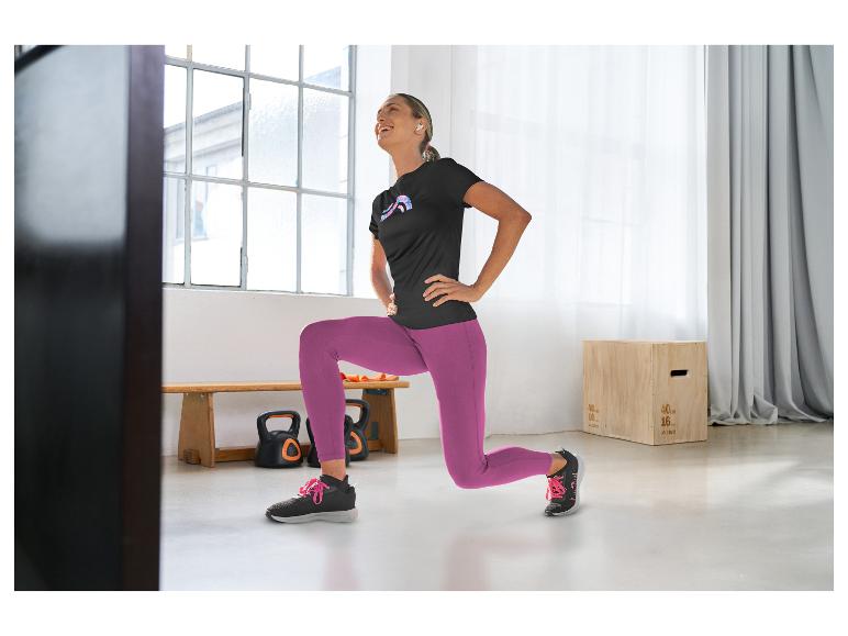 Femme en t-shirt de sport noir et leggings violets faisant des fentes dans une salle de sport.