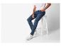 Homme en T-shirt blanc et jean bleu assis sur un tabouret blanc.