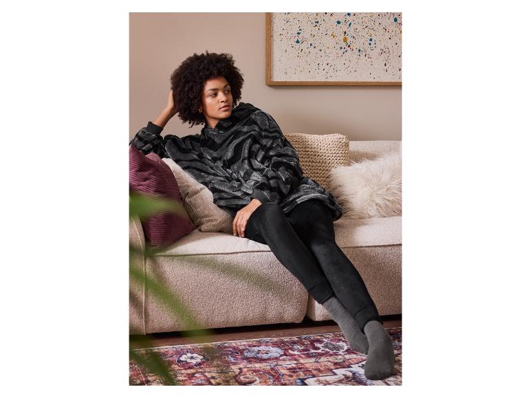 Femme en sweat à capuche zébré gris et leggings noirs se relaxant sur un canapé.