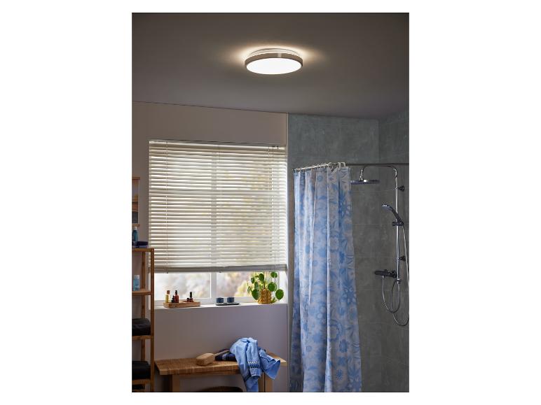 Un luminaire de salle de bain rond avec un abat-jour blanc dans une salle de bain avec un rideau de douche.