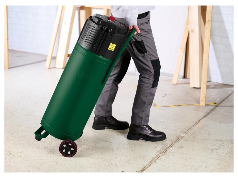 Homme tirant un aspirateur industriel vert à roulettes, avec étiquette 96 dB.