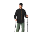 Homme en polaire noire, pantalon de randonnée vert et bonnet, tenant des bâtons de marche.