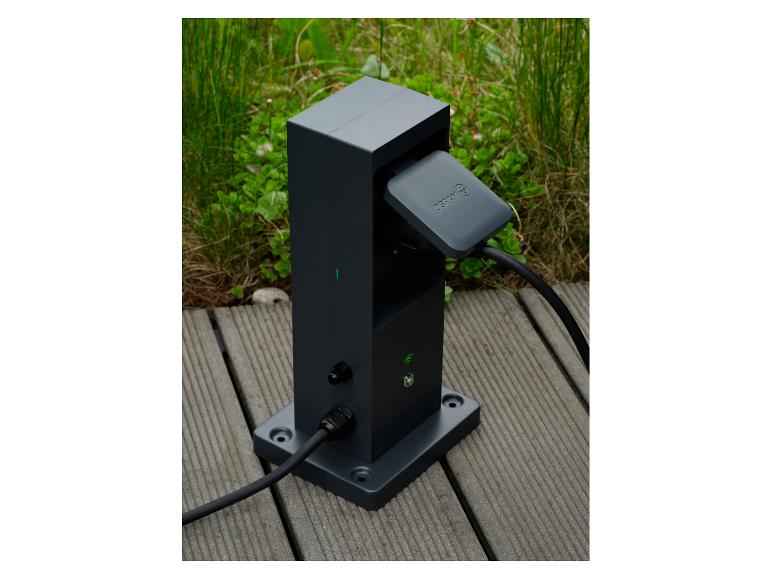 Borne de recharge gris foncé pour véhicules électriques avec câble branché sur une terrasse en bois.