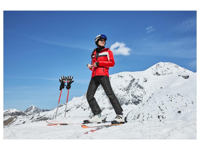 Skieuse en veste rouge, pantalon noir, casque et lunettes en montagne.