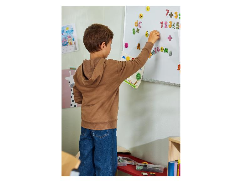 Enfant plaçant des lettres et chiffres magnétiques colorés sur un tableau blanc.