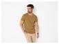 Homme en t-shirt marron et pantalon beige, la main dans la poche.