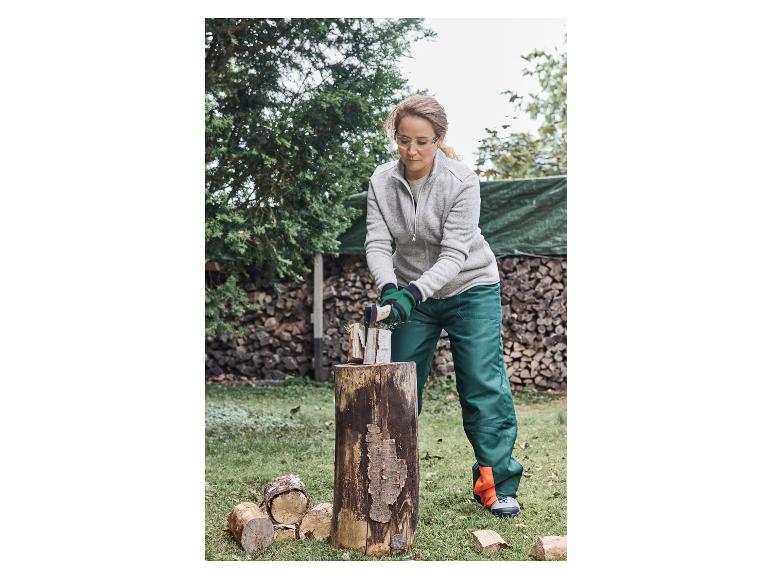 Femme avec des lunettes de sécurité et des gants fendant du bois à la hache.