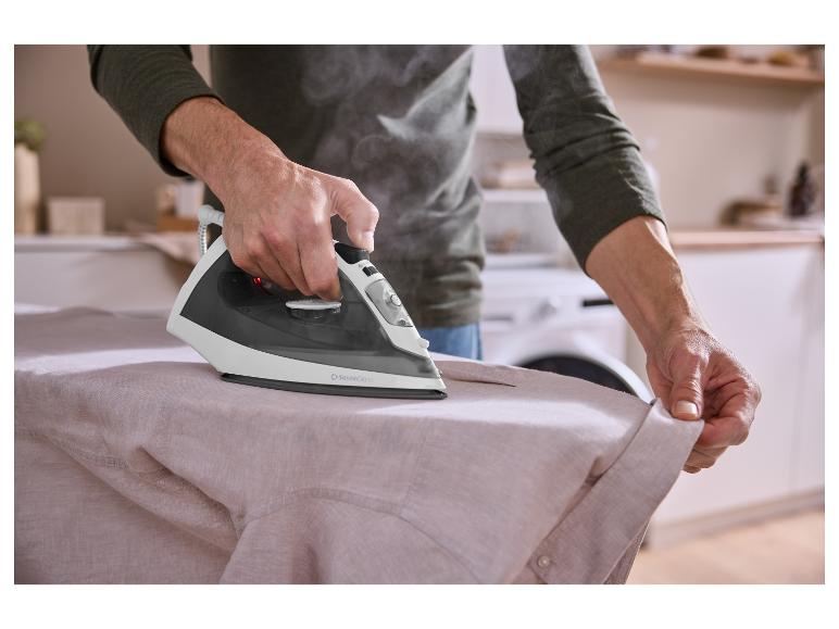 Une personne repassant une chemise claire avec un fer à vapeur SilverCrest, vapeur visible.