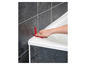 Une main utilise un outil de calfeutrage en silicone rouge pour enlever le calfeutrage autour d'une baignoire.