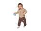 Bébé souriant portant une veste beige et un pantalon marron, tenant un hochet.