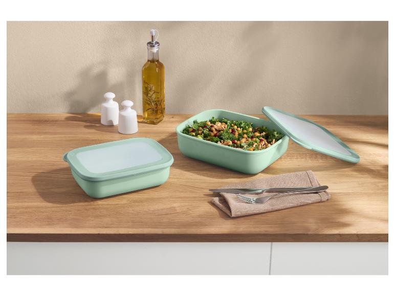Deux boîtes alimentaires menthe, une avec salade, sur un comptoir en bois avec huile et assaisonnements.