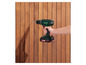 Une main tenant une perceuse Parkside X20V verte, perçant un mur en bois.