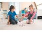 Deux enfants jouent avec un chiot robot blanc et rose sur le sol.