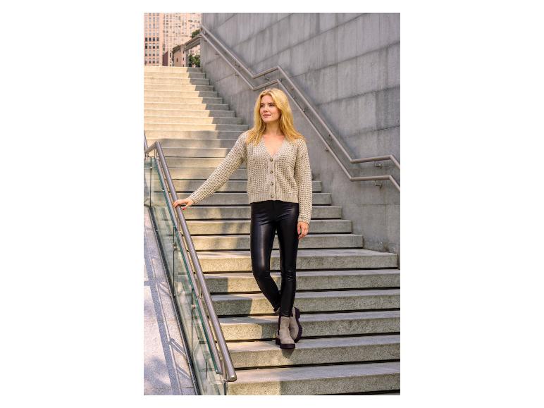 Femme en cardigan beige et leggings en similicuir noir sur des escaliers en béton.
