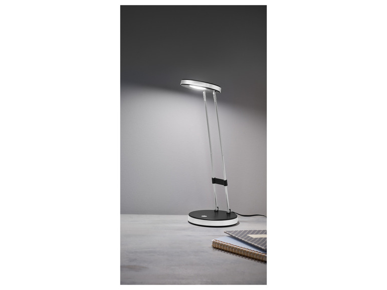 Une lampe de bureau argentée avec un abat-jour rond, sur un bureau avec un carnet.