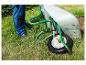 Une brouette verte avec une roue, un tuyau d'arrosage et un arroseur dans un jardin vert.