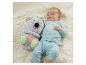 Bébé souriant allongé à côté d'une peluche koala lumineuse sur un tapis moelleux.