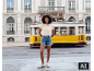 Femme en t-shirt beige ajouré et short en jean devant un tramway jaune.