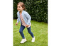 Une fille porte une veste bleue, un t-shirt rose à imprimé pastèque, un legging bleu et des baskets blanches.