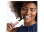 Une femme utilise une brosse à dents électrique rose.