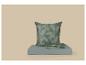 Coussin vert et linge de lit plié à motif de feuilles sur une surface bleu clair.