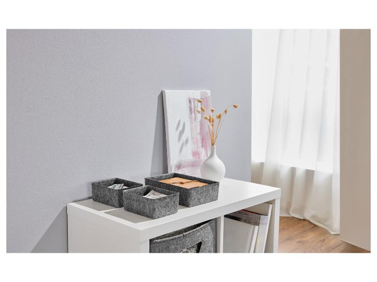 Boîtes en feutre grises sur étagère blanche avec décorations.