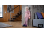 Enfant en bas âge en pull rose et leggings appuyé contre un mur en bois.