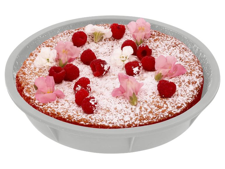 Gâteau avec sucre glace, framboises et fleurs dans un plat gris.