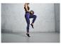 Une femme en leggings bleus et en chaussures de sport noires tient un ballon de fitness.